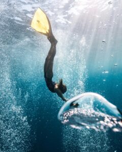 A scuba diver gracefully descends through clear Indonesian waters, surrounded by bubbles.