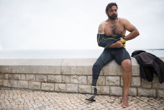 Man with prosthetic leg in wetsuit sitting by a stone ledge outdoors.